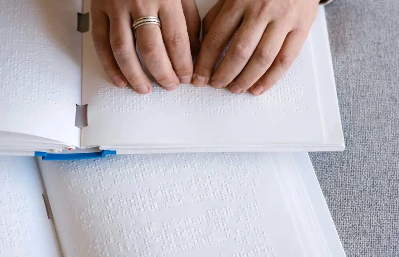 Hands reading Braille text on an open book, representing tactile reading and accessibility.